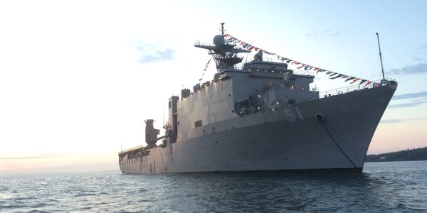 Large naval ship decorated with signal flags at sunset on calm waters.