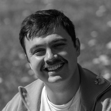A man with a mustache smiling in a close-up black and white photo.