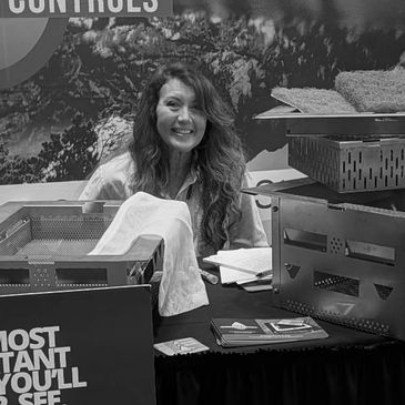 Smiling woman at a booth with promotional materials and equipment.