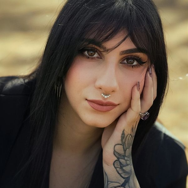 Close-up of a woman with dark hair, septum piercing, and tattooed hand.