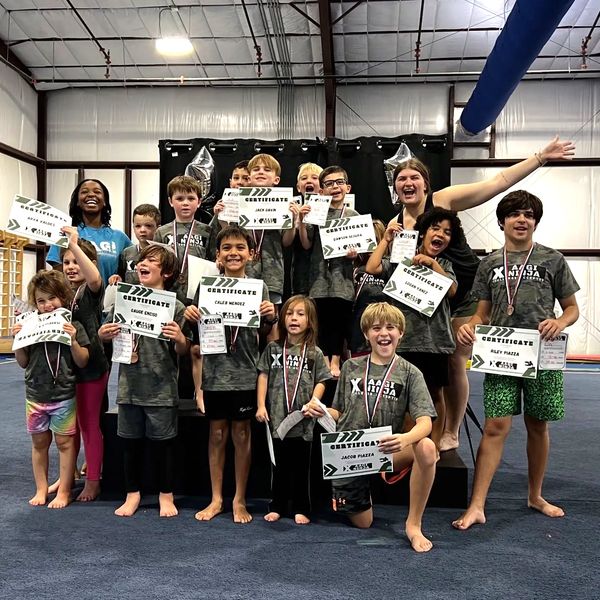 Group of kids and their coach proudly holding certificates and medals in a gym.