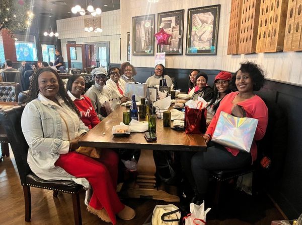 A joyful group of women gathered around a restaurant table with gifts and drinks.