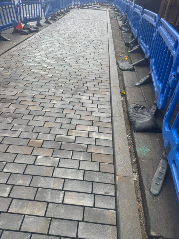 Newly paved sidewalk with blue safety barriers.