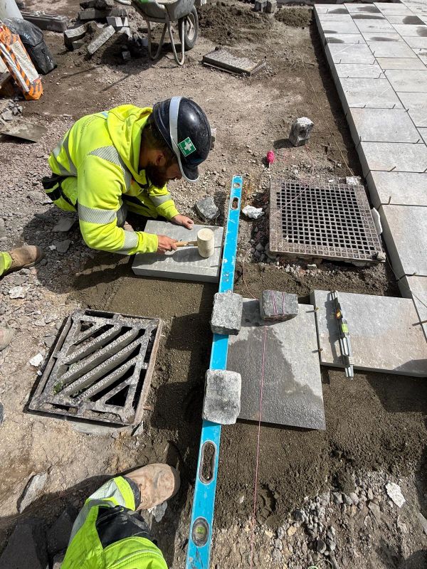 Construction worker setting paving stones with tool and level.