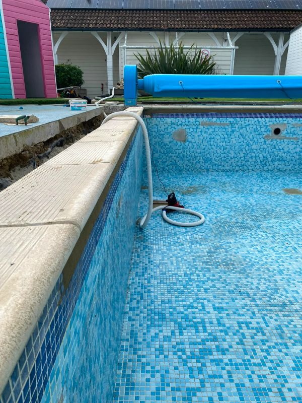 Empty pool with cleaning equipment and exposed ground nearby.