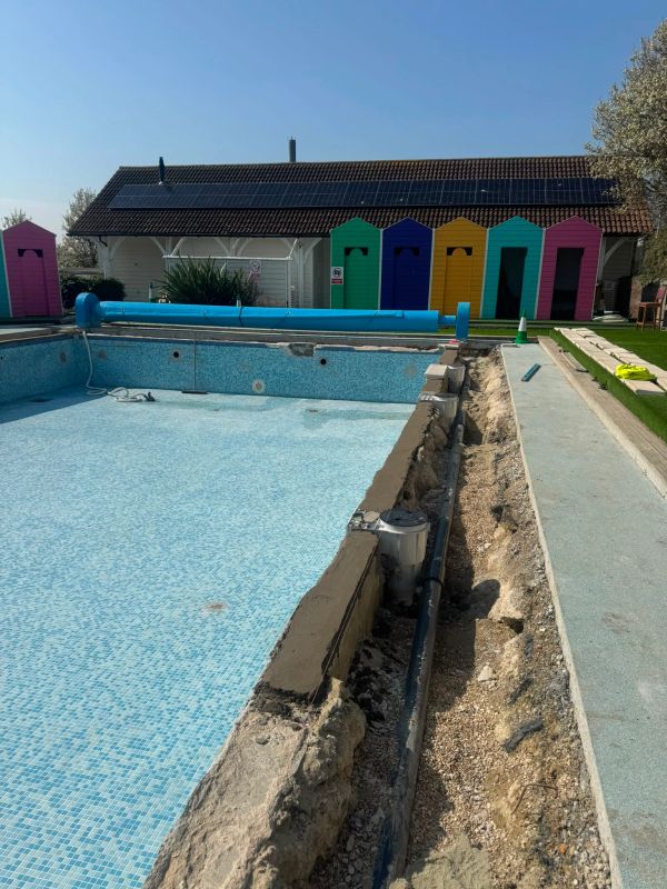 Empty pool under repair with colorful changing rooms behind.