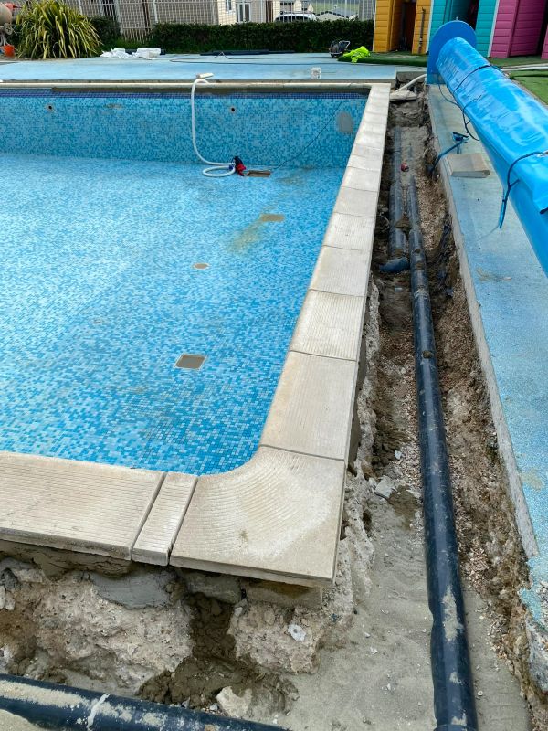 Empty tiled swimming pool under maintenance with exposed pipes.