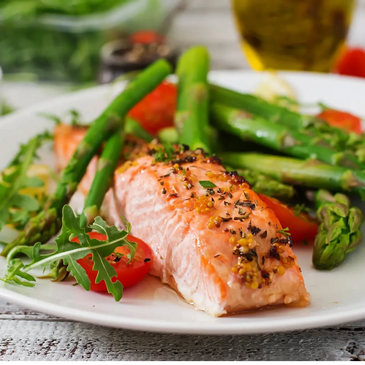 Grilled salmon fillet with asparagus and cherry tomatoes on a white plate.