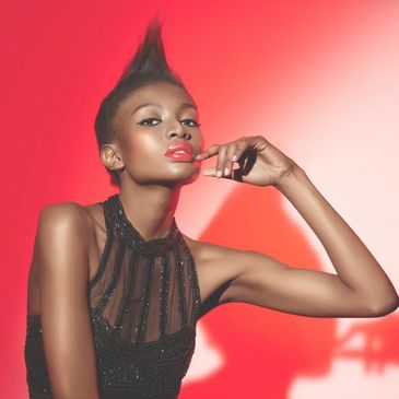 Elegant woman with mohawk hairstyle posing against a red background.