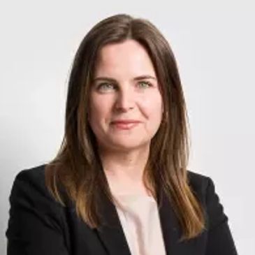 Confident woman in a black blazer standing with arms crossed against a plain background.