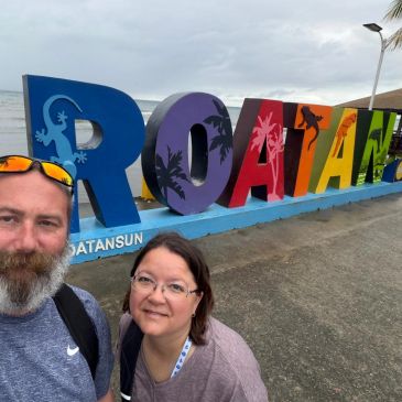 Two people posing in front of colorful Roatan sign.