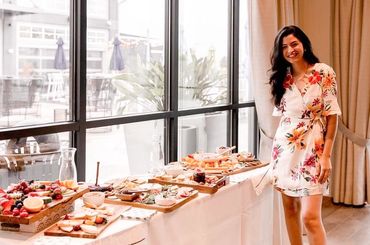 Woman in floral dress standing next to a table filled with elegant appetizers.