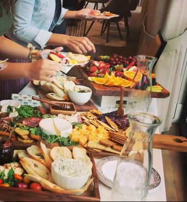People serving themselves from a vibrant, diverse charcuterie spread at a gathering.