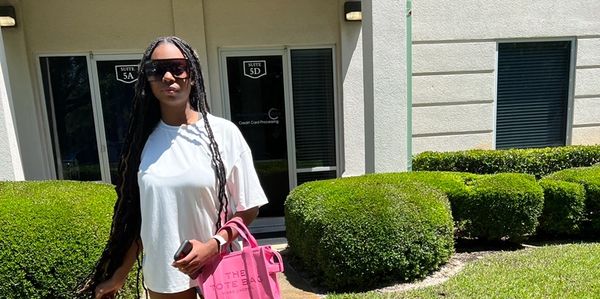 Woman in white shirt with long braids and pink bag outdoors.