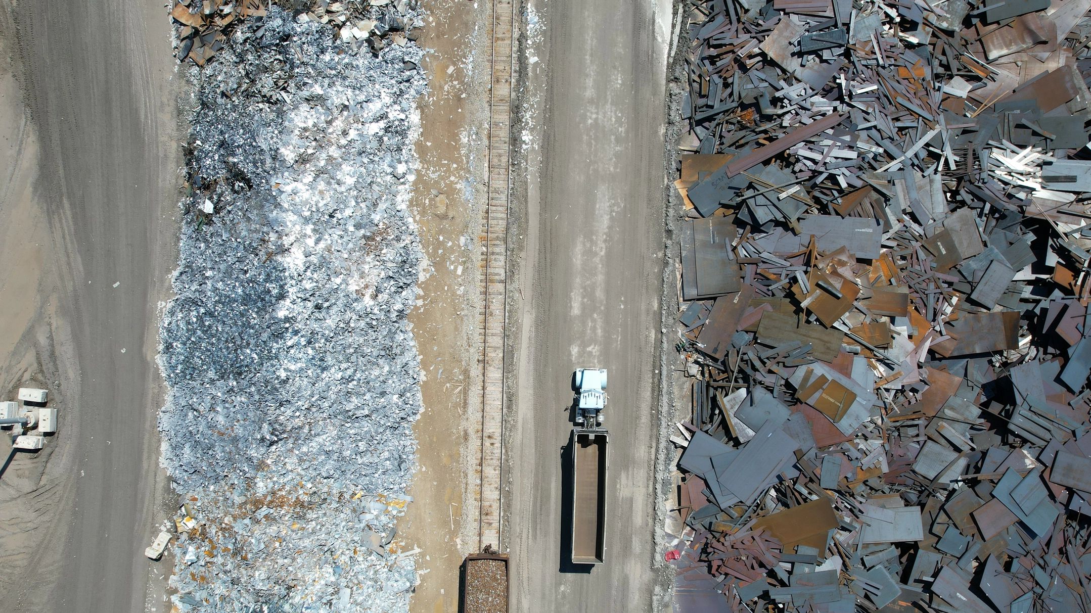 Aerial view of a truck driving between two piles of scrap metal.