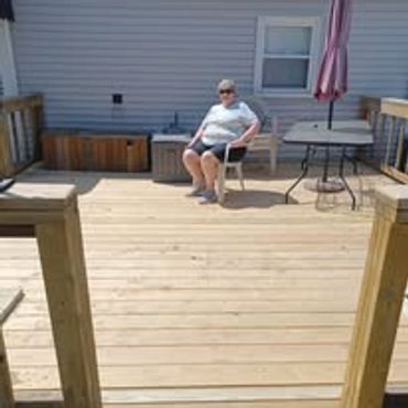 Person sitting on chair on wooden deck outside a house.
