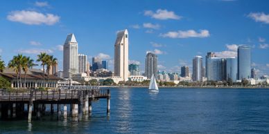 San Diego skyline with sailboat and waterfront pier under a bright blue sky.