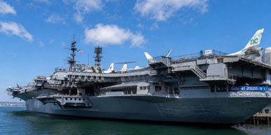 A large aircraft carrier docked under a blue sky.