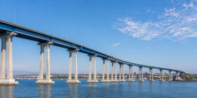 Long concrete bridge over calm water under a blue sky.