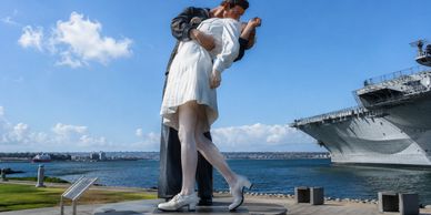 Statue of a sailor kissing a nurse by the waterfront with a ship in the background.