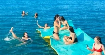 Group of women enjoying swimming and relaxing on a floating platform in clear blue water.