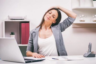 Woman stretching neck at desk with laptop.