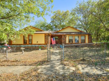 Single-story house with yellow and brick exterior behind a chain-link fence.