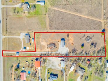 Aerial view of a rectangular plot of land outlined in red with a building and open fields.