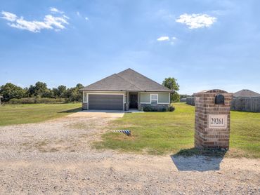 A single-story house with a large lawn and brick mailbox under a clear blue sky.