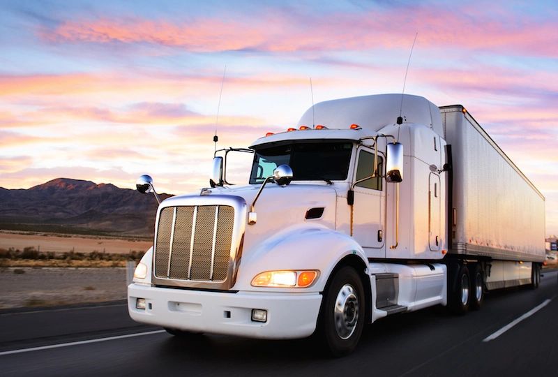 Large, white semi on highway with sunset a mountain the backdrop.