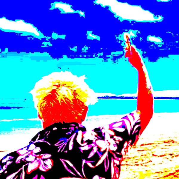Person with dyed hair on beach, raising hand against a vivid blue sky.