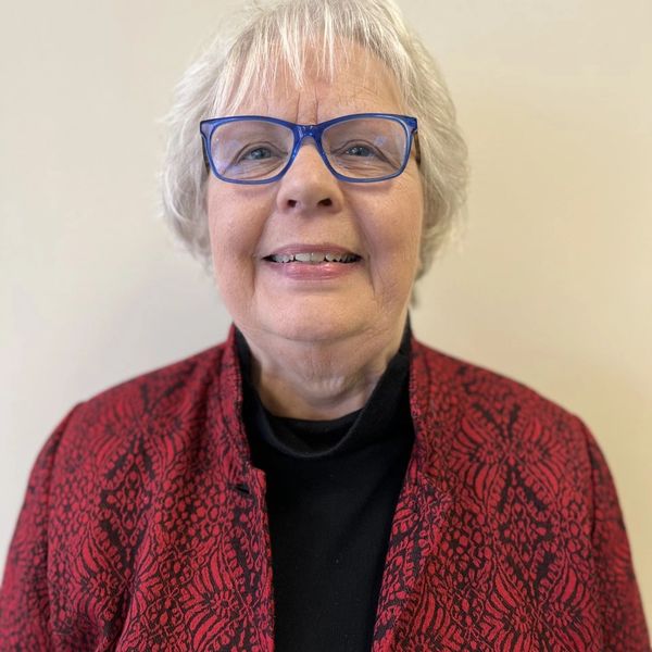 Diane Andert with blue glasses and a red shirt smiling and looking very friendly.