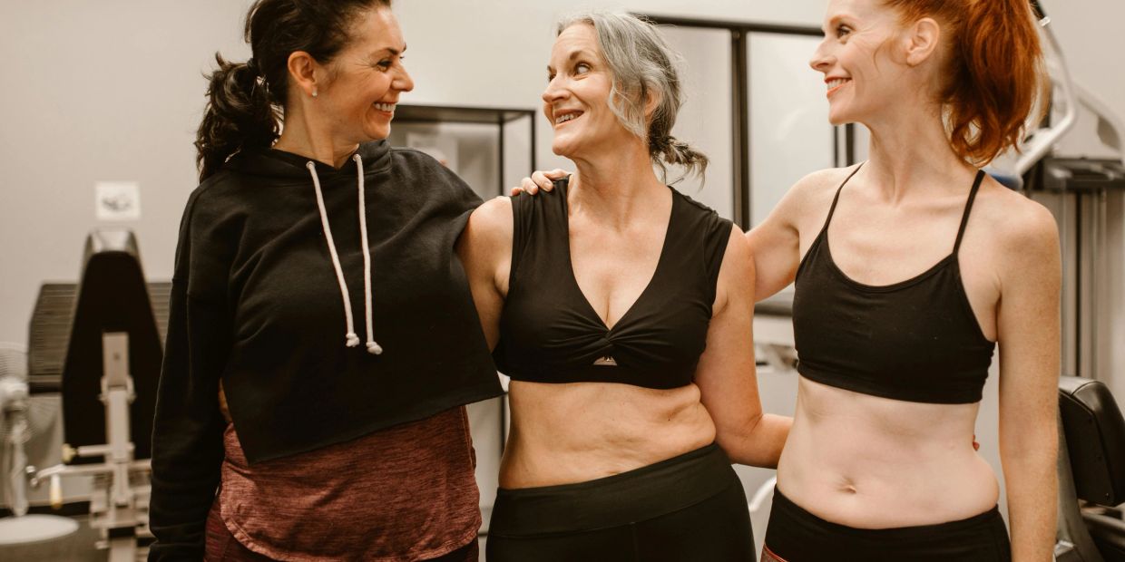 Three women smiling and supporting each other in a gym setting.