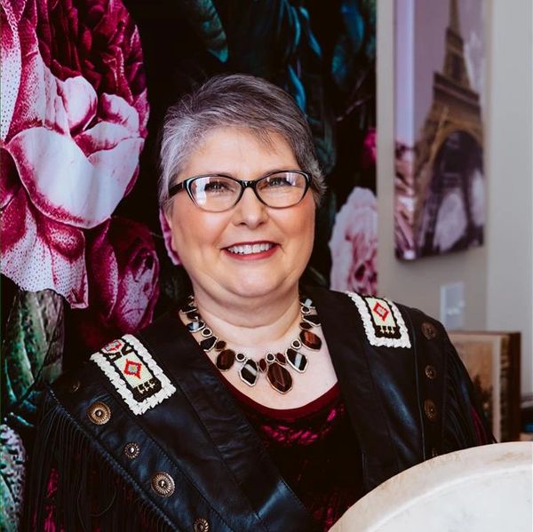 Photo of Samantha Sieverling standing in front of a floral wall in a black and red outfit with beads