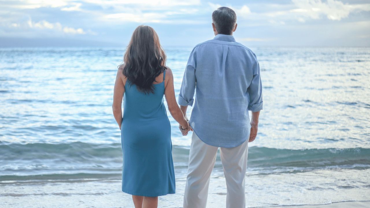 a couple holding hands on the beach looking at the ocean