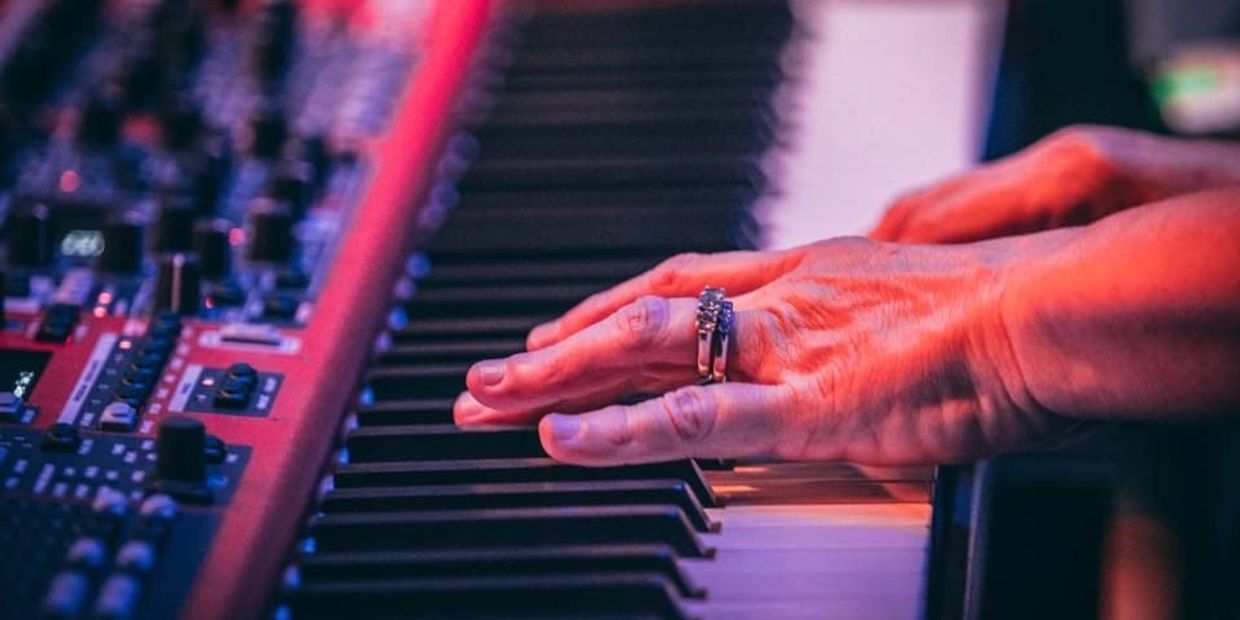 Hands playing a keyboard synthesizer with colorful lighting.