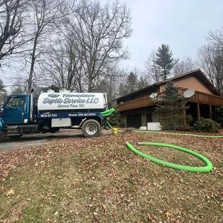 Septic service truck parked beside a house with hose laid out.