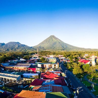 A town with colorful rooftops nestled near a large volcano under a clear blue sky.