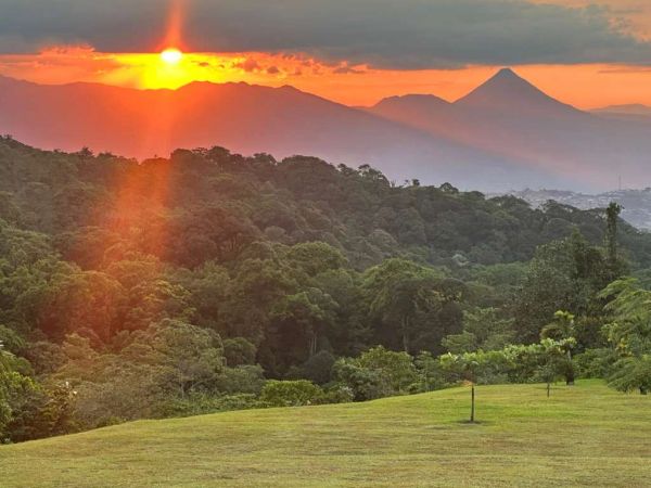 Sunset over lush green hills and distant mountains.