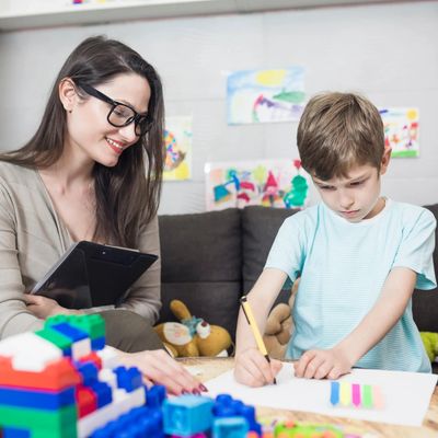 Educational School Psychologist sits next to child drawing a picture. Assessing for disabilities.