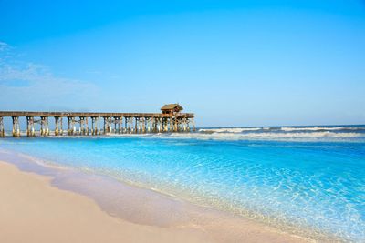 Clear blue ocean with a wooden pier stretching into the water under a bright sky.