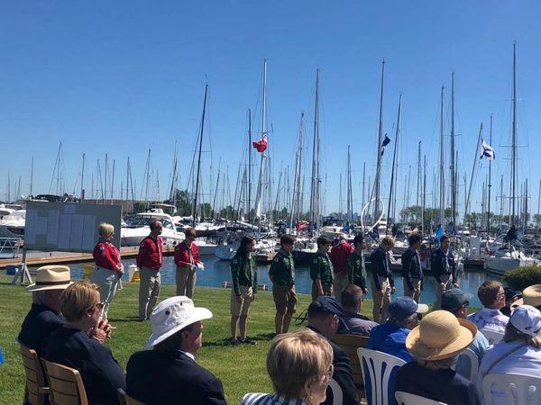 A group of scouts and audience at a marina event on a sunny day.