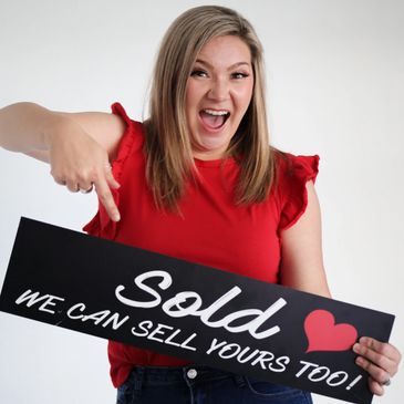 Excited girl in a red shirt with open mouth, holding a real estate sign that says 'Sold..."