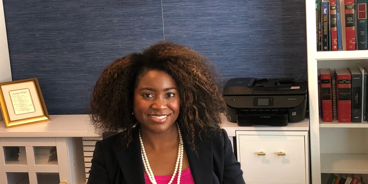 Smiling woman with curly hair sitting at desk, wearing a pearl necklace.