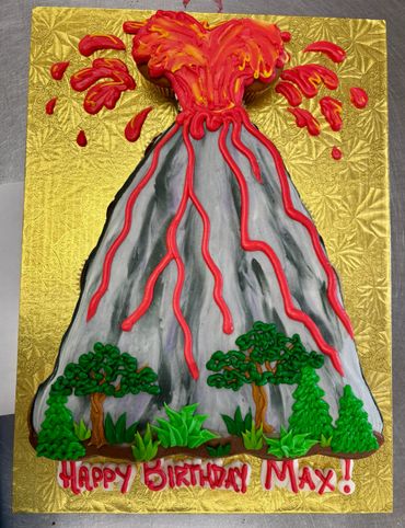 Volcano-shaped birthday cake erupting with red lava and surrounded by trees.