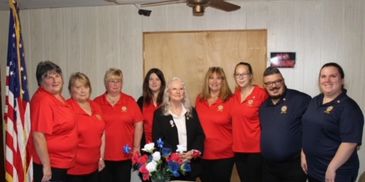 Group of people in red and navy shirts posing indoors with American flag.