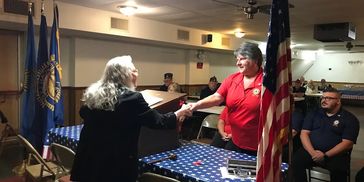 Two women shaking hands at a podium in a veterans hall.