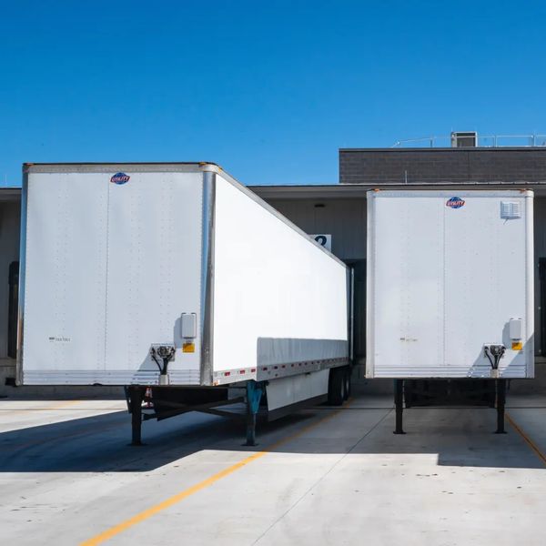 Two white semi-truck trailers parked side by side at a loading dock.