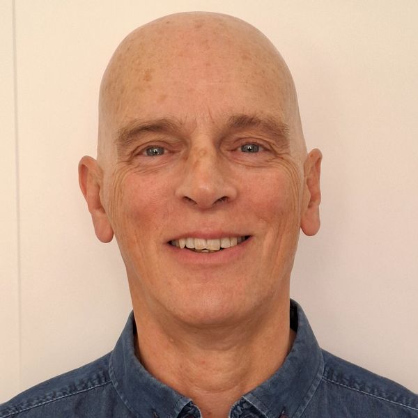 Smiling bald man in a blue shirt against a plain background.