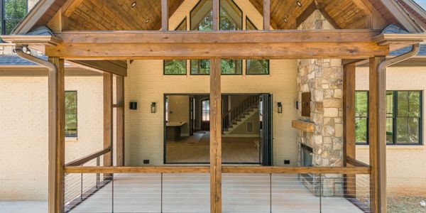 Wooden deck with stone fireplace and large glass doors in a modern rustic home.